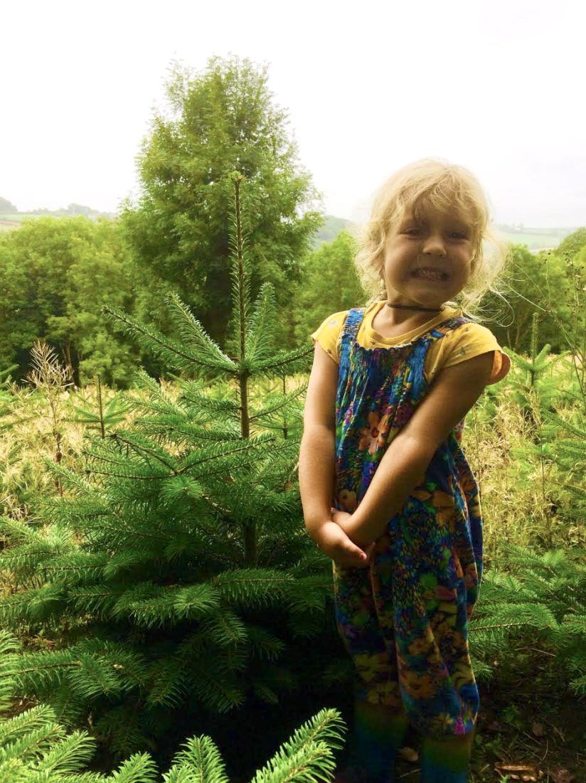 A young girl smiling next to a growing Christmas tree on the farm
